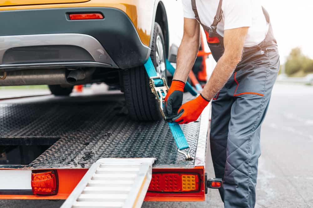 A person who is a professional in vehicle towing fixing a strap on a car
